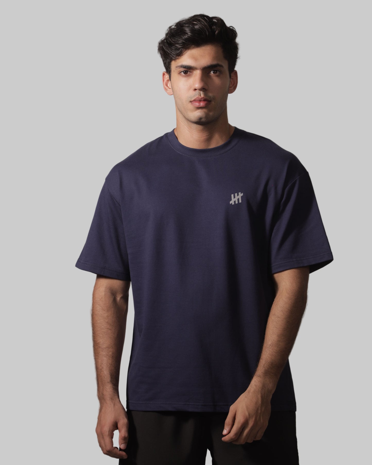 Man wearing a navy blue t-shirt with a logo on a plain background